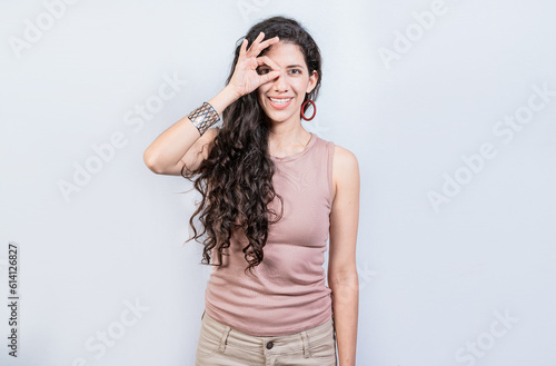 Happy young girl making ok gesture with hand looking through fingers. Friendly girl doing ok gesture looking through fingers