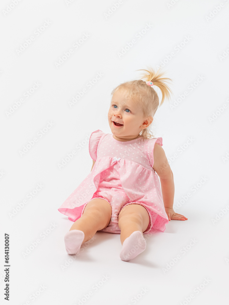 Surprise, delight.A cute blonde girl 1-2 years old in a pink dress is sitting on the floor with her mouth open on a white background. Copy space. Surprise, delight.A cute blonde girl 1-2 years old in a pink dress is sitting on the floor with her mouth open on a white background. Copy space.