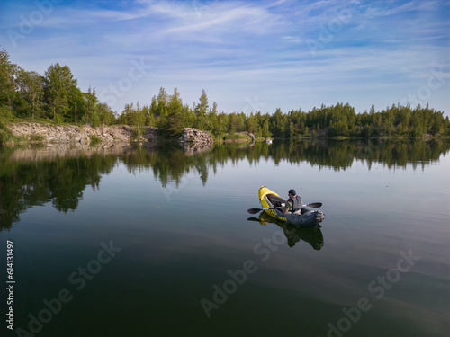 A man in a kayak swims on a forest lake on a summer morning.