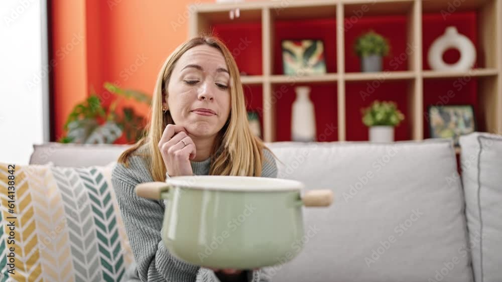 Young blonde woman holding cooking pot for water leak at home