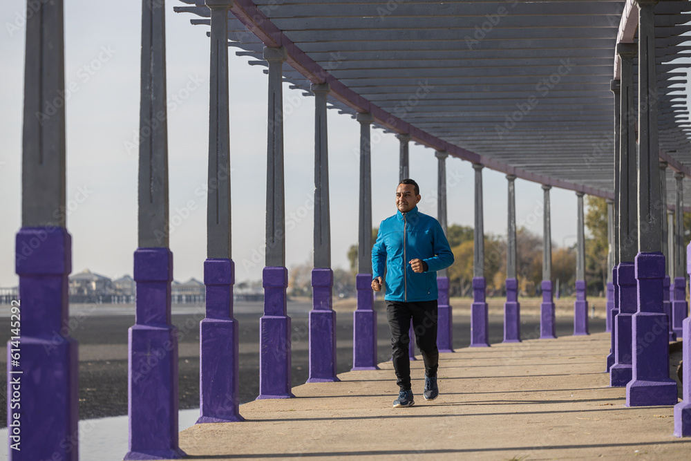 Young Latino man runs by a pergola in a park. Young Latino man runs by a pergola in a park.