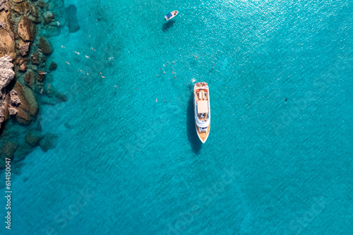 Aerial top down view of a swimming tourists and yacht anchored in the turquoise sea © kirill_makarov