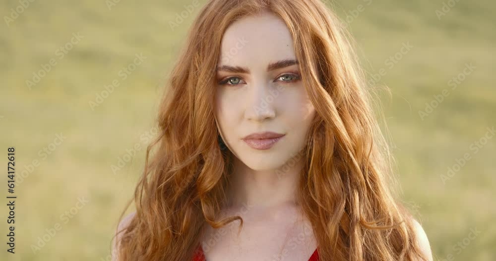 Close-up portrait of young fashionable caucasian ginger woman posing outdoors. Face young ginger woman look at camera stand in field summer beautiful lady portrait happy outdoor close up slow motion Close-up portrait of young fashionable caucasian ginger woman posing outdoors. Face young ginger woman look at camera stand in field summer beautiful lady portrait happy outdoor close up slow motion