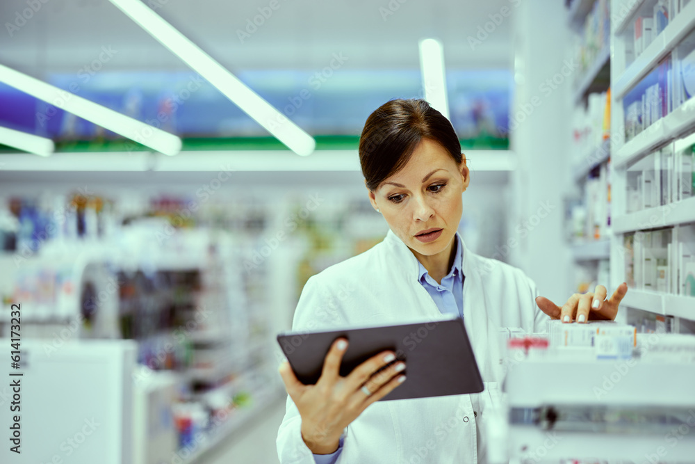 Fototapeta premium A busy female pharmacist doing an inventory and looking at the tablet.