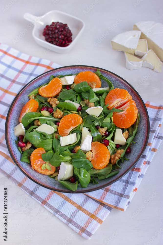 Top view of tangerine salad with mixed leaves, Camembert and walnuts in a grey bowl on cotton chessboard pattern napkin. Placed on white background. Healthy food concept