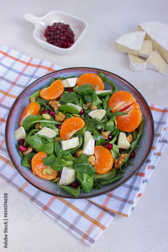 Top view of tangerine salad with mixed leaves, Camembert and walnuts in a grey bowl on cotton chessboard pattern napkin. Placed on white background. Healthy food concept Top view of tangerine salad with mixed leaves, Camembert and walnuts in a grey bowl on cotton chessboard pattern napkin. Placed on white background. Healthy food concept