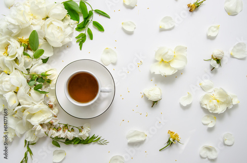 Delicate flower composition of tea with white roses and petals with acacia flowers on white background. Top view.
