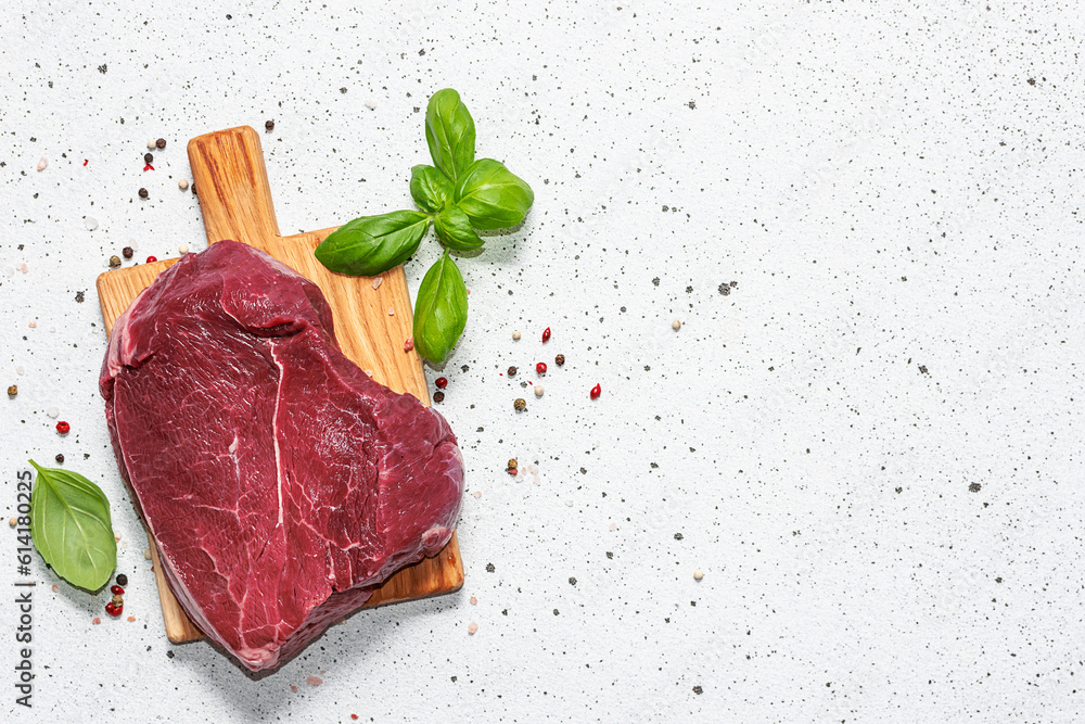 Raw beef steak with spices and herbs on white marble background with copy space for your design.