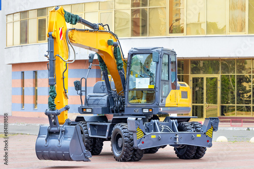 New wheeled construction excavator against the backdrop of a building on a sunny day.