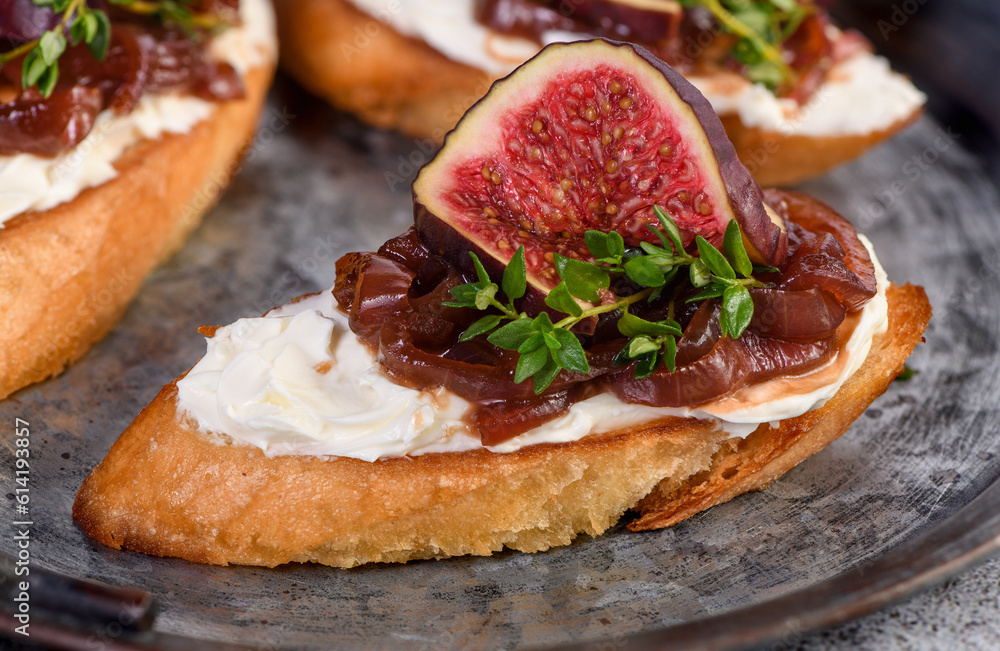  Canape or crostini with toasted baguette, cream cheese, onion jam, figs and fresh thyme on a tin tray. Ideal appetizer as an aperitif.