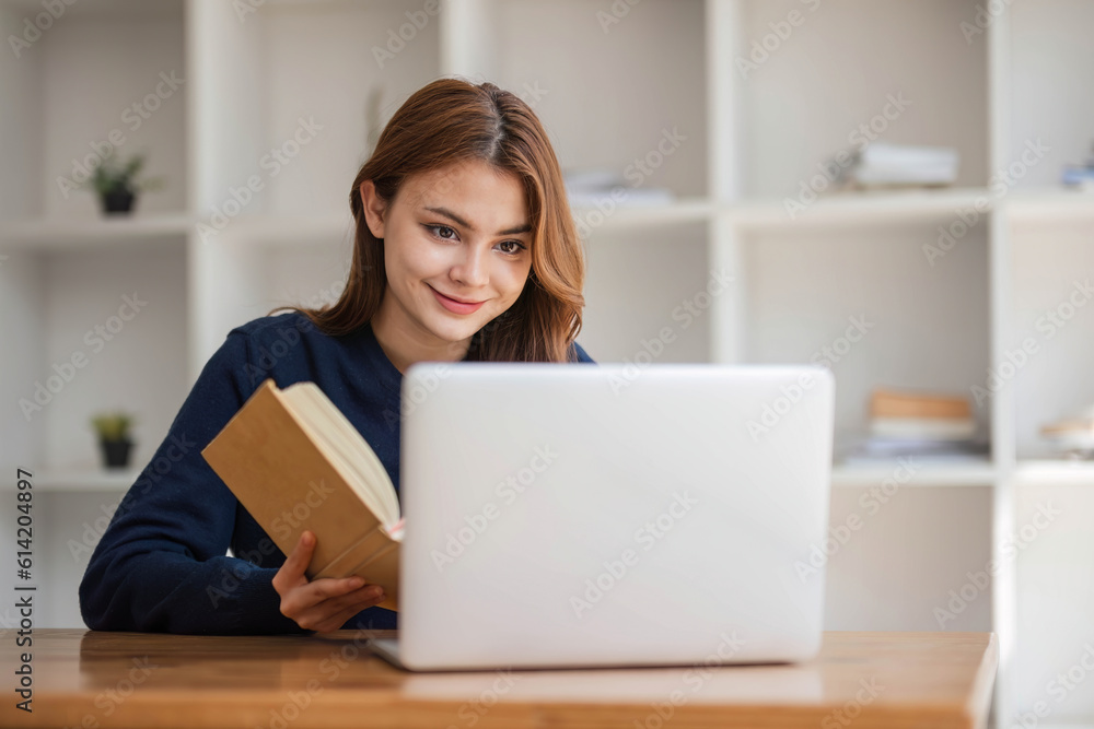 Smiling asian undergraduate teen girl student study in library with laptop books doing online research for coursework, making notes for essay homework assignment, online education e-learning concept Smiling asian undergraduate teen girl student study in library with laptop books doing online research for coursework, making notes for essay homework assignment, online education e-learning concept