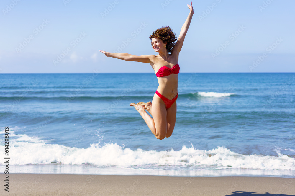 Happy woman in bikini jumping in air on beach Happy woman in bikini jumping in air on beach