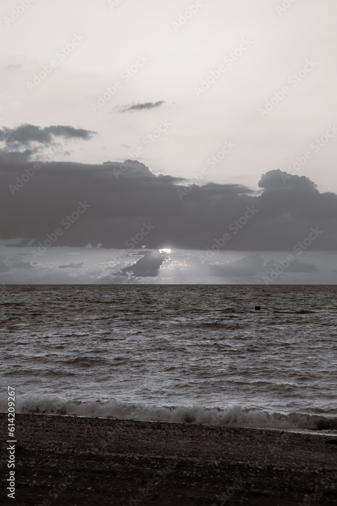 Sun shinning through the clouds at sunset at Paralia Ixia beach off Rhodes city in black and white
