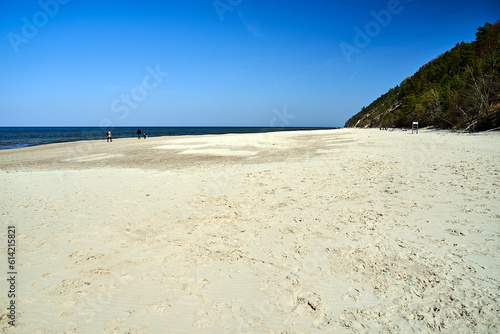 People walking on a sandy beach with trees on a cliff on the island of Wolin