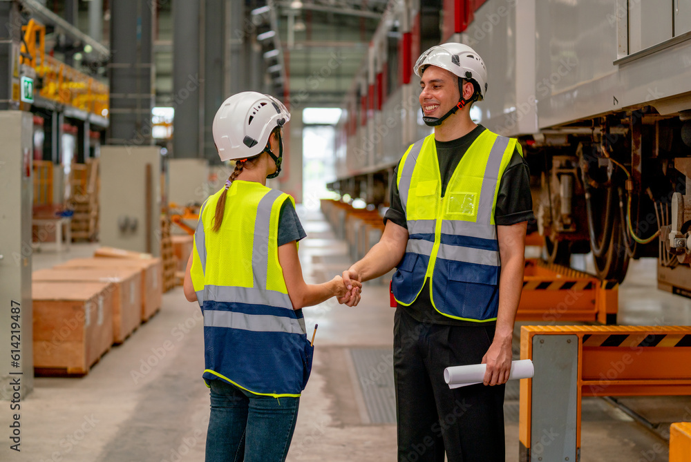 Engineer or factory technician worker man and woman shake hands for the success of joined project together in workplace near the electric train on rail. Engineer or factory technician worker man and woman shake hands for the success of joined project together in workplace near the electric train on rail.
