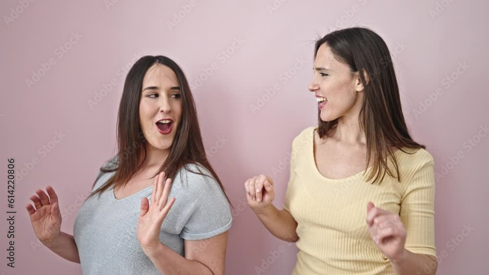 Two women smiling confident dancing over isolated pink background Two women smiling confident dancing over isolated pink background