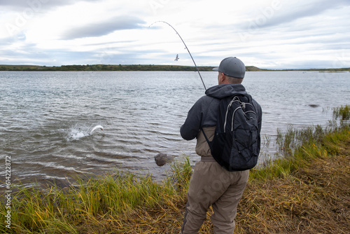 A coho salmon jumps in the Egegik river in Alaska as a man fights the fish with his bent rod