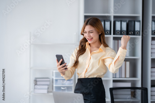 Happy businesswoman raising hands with victory smiling happily with smart phone. The concept of success at work.