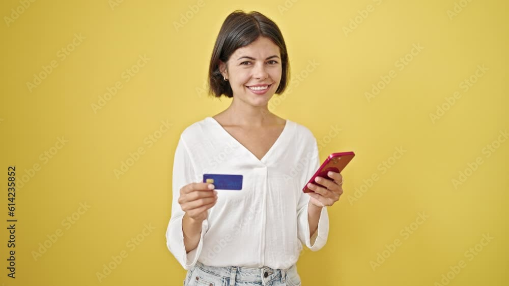 Young beautiful hispanic woman shopping with smartphone and credit card over isolated yellow background Young beautiful hispanic woman shopping with smartphone and credit card over isolated yellow background
