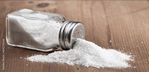 Tableau sur toile Salt glass jar and pile of spilled salt on a wooden table