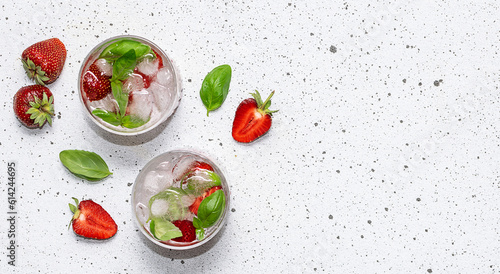 Fresh iced lemonade with strawberry and basil on the serving board on white marble background top view, copy space for your design.