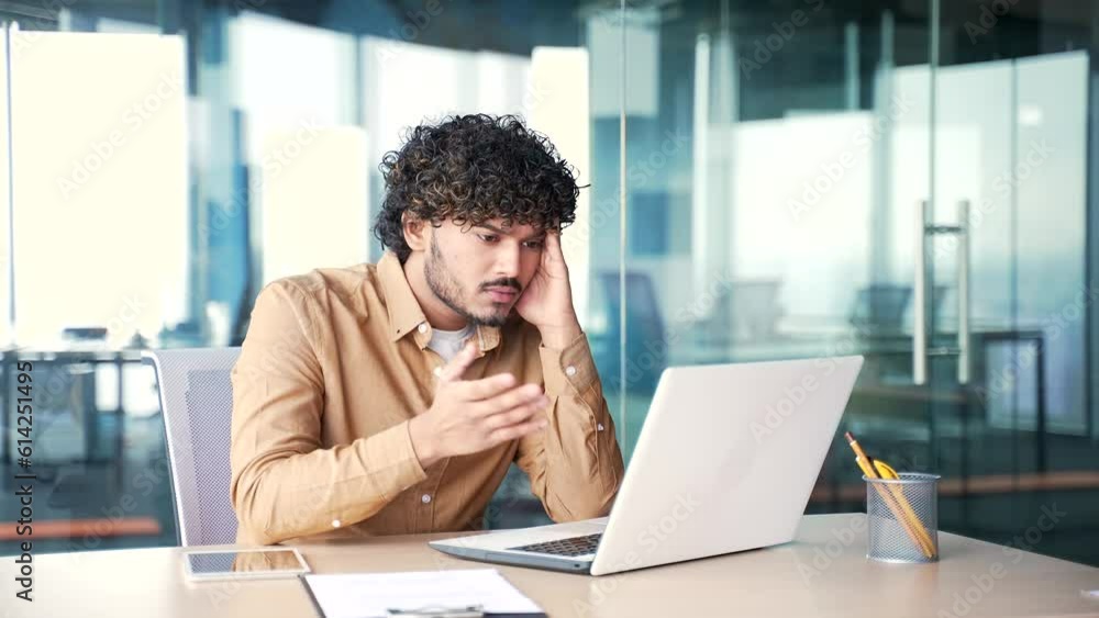 Frustrated stressed young employee reads bad news on laptop while sitting at workplace in modern office. Worried male worker is sad, has a bad mood while reviewing negative information on computer Frustrated stressed young employee reads bad news on laptop while sitting at workplace in modern office. Worried male worker is sad, has a bad mood while reviewing negative information on computer