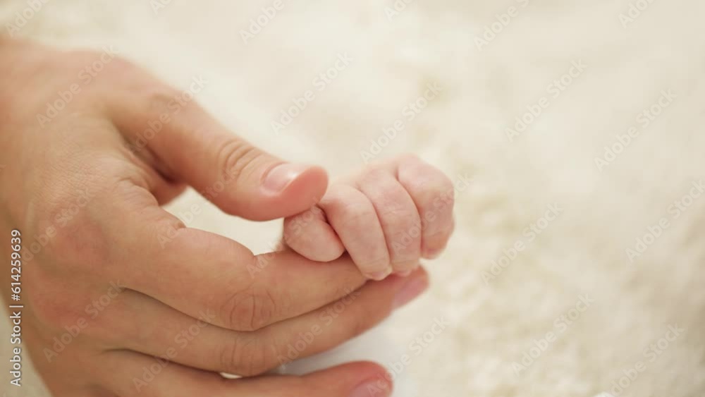 The newborn baby holds onto her mother's finger. The mother gently strokes the baby's hand with her finger. Motherhood. Close up The newborn baby holds onto her mother's finger. The mother gently strokes the baby's hand with her finger. Motherhood. Close up