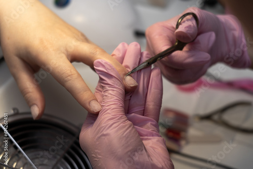 Classical manicure. Hygiene and care for hands, beauty industry concept. Woman manicurist master is cutting cuticle using scissors on client's finger in beauty salon, closeup hands view.
