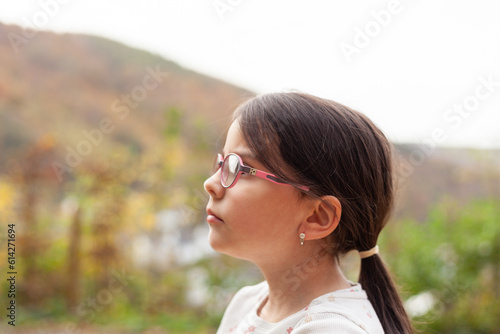 Portrait of a little girl with long hair wearing glasses and looking away