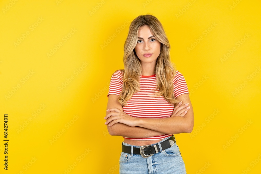 Serious pensive Young beautiful woman wearing striped t-shirt over yellow background feel like cool confident entrepreneur cross hands. Serious pensive Young beautiful woman wearing striped t-shirt over yellow background feel like cool confident entrepreneur cross hands.