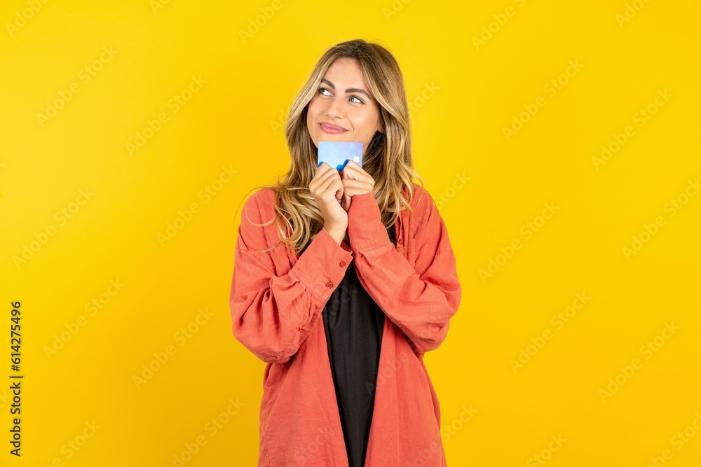 Photo of cheerful young beautiful blonde woman standing over yellow studio background hold debit card look empty space Photo of cheerful young beautiful blonde woman standing over yellow studio background hold debit card look empty space