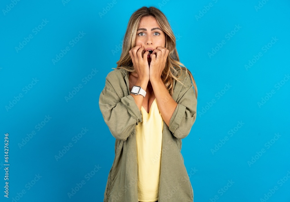 Speechless young beautiful blonde woman standing over blue studio background keeps hands near opened mouth reacts to shocking news stares wondered at camera Speechless young beautiful blonde woman standing over blue studio background keeps hands near opened mouth reacts to shocking news stares wondered at camera