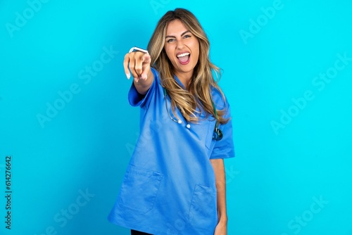 Young beautiful doctor woman standing over blue studio background pointing displeased and frustrated to the camera, angry and furious ready to fight with you.