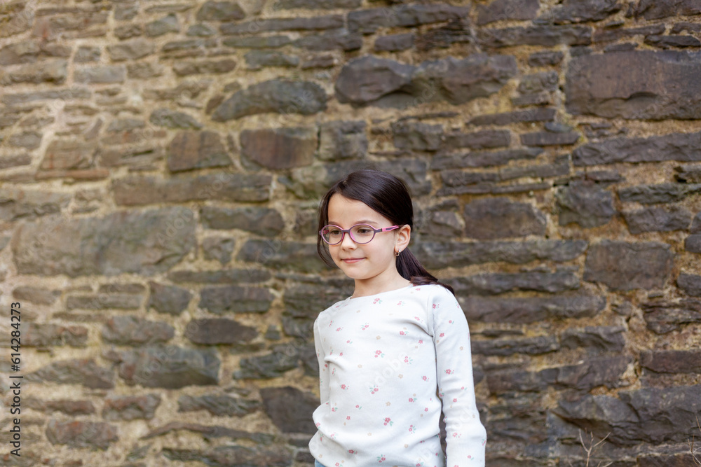 Portrait of a little girl in glasses against a stone wall. Portrait of a little girl in glasses against a stone wall.