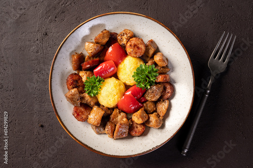 Delicious traditional romanian dish pomana porcului assortment of pork meat and sausages with mamaliga and pickled red peppers in a plate on dark background. Top view. photo