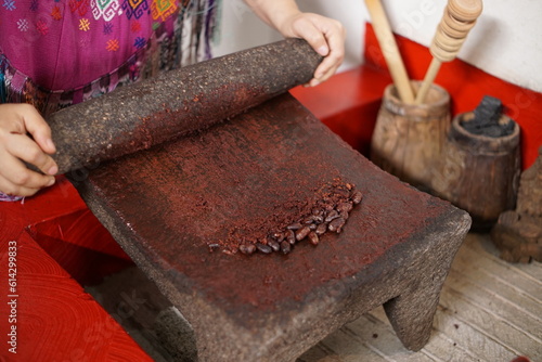 Guatemalan mayan woman making chocolate with traditional grinding stone photo