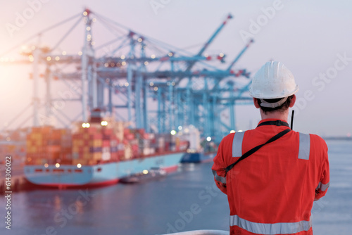 Offshore technician. Seafarer. Seaman. Navigator. A man in a boiler suit is standing in front of the port. Seafarer in front of the container terminal.  © Andriy Sharpilo