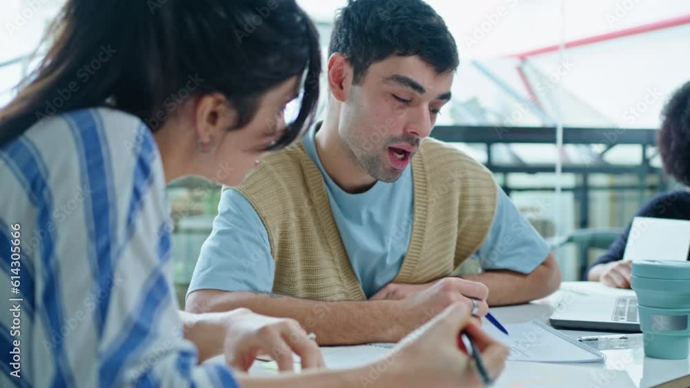 Young man and woman sitting together at meeting table in the office, discussing business papers and making notes, cooperating during working day Young man and woman sitting together at meeting table in the office, discussing business papers and making notes, cooperating during working day