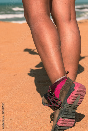 Footprints in the Sands: Female Feet in Trekking Boots Walking on Sunny Desert Beach