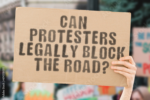 A thought-provoking image of a man's hand holding a banner with the text 'Can protestors legally block the road?' Perfect for showcasing support or protest
