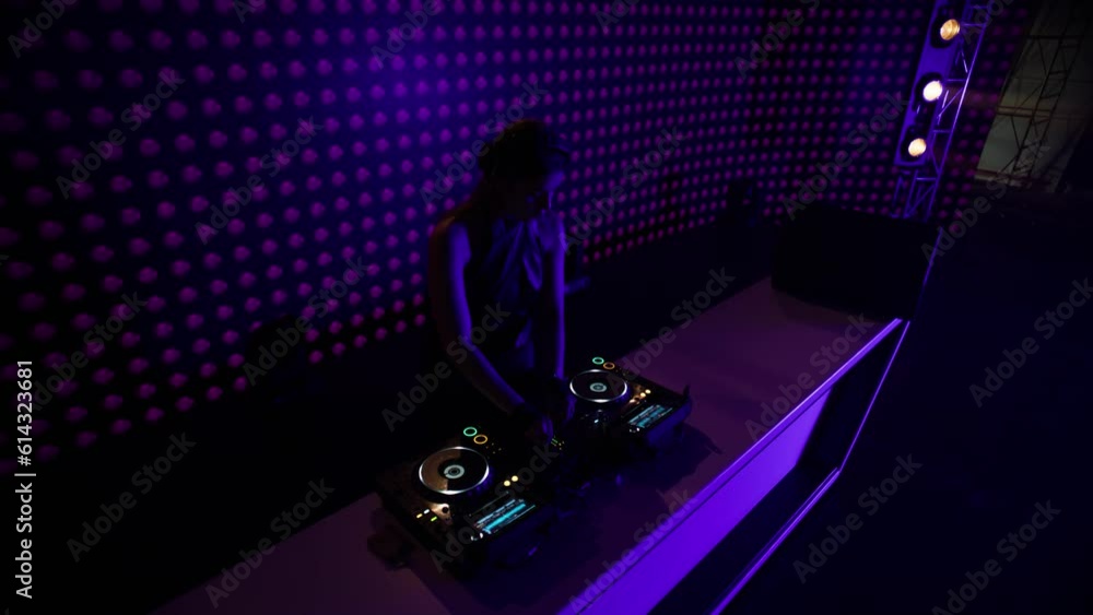 Portrait of attractive female techno DJ performing playing her music set on a stage of a nightclub or during a festival, bright flashing stage lights, huge LED screen behind talent Portrait of attractive female techno DJ performing playing her music set on a stage of a nightclub or during a festival, bright flashing stage lights, huge LED screen behind talent