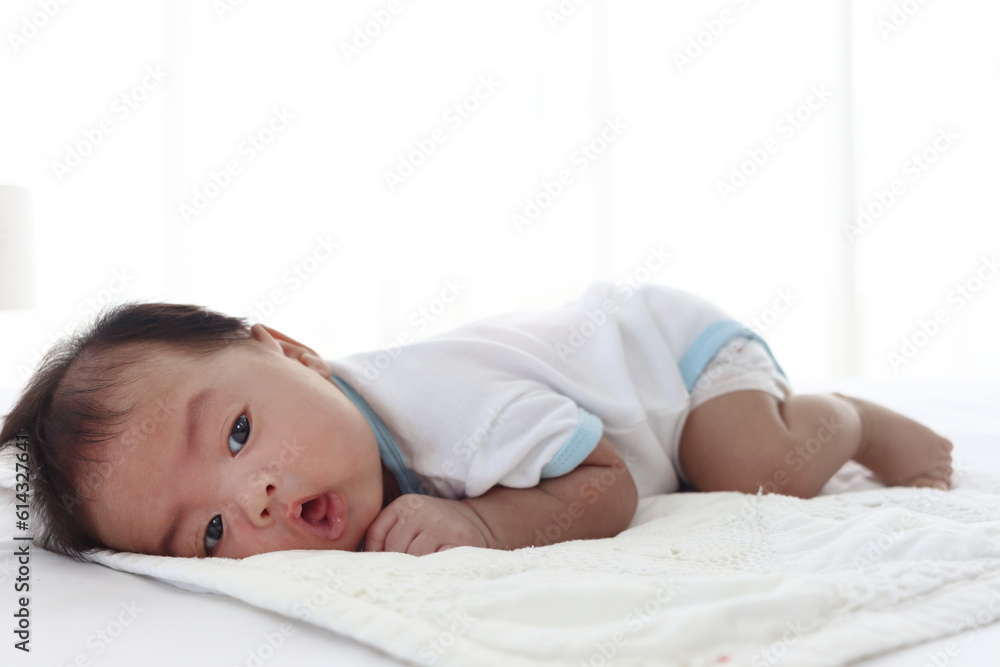 Cute happy newborn infant baby boy lying down on white bed in bedroom, lovely child sleeping on stomach, nursery for kid children family concept. Cute happy newborn infant baby boy lying down on white bed in bedroom, lovely child sleeping on stomach, nursery for kid children family concept.