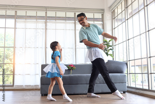 Cute little girl with young cheerful handsome dad wearing beautiful skirt and dancing together  dad trying to train his daughter to dance ballet  Happy family spending time together. Happy Father Day.