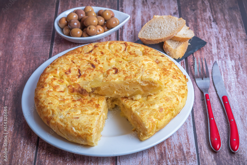 typical spanish potato omelette freshly made on a wooden table with cutlery, bread and olives. typical spanish potato omelette freshly made on a wooden table with cutlery, bread and olives.