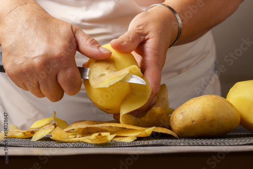 close-up of a woman's hands in a white apron peeling potatoes with a knife.