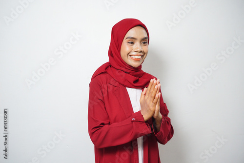 Asian Muslim businesswoman in red casual giving greeting with both hands isolated on white background