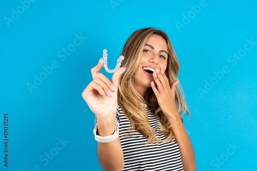 Happy Young beautiful woman wearing striped t-shirt holding and showing at camera an invisible aligner while laughing. Dental healthcare and confidence concept.