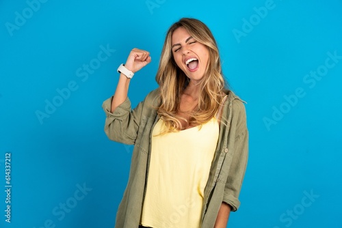 Portrait of funny young beautiful blonde woman wearing overshirt shout yeah raise fists hands celebrate victory game competition