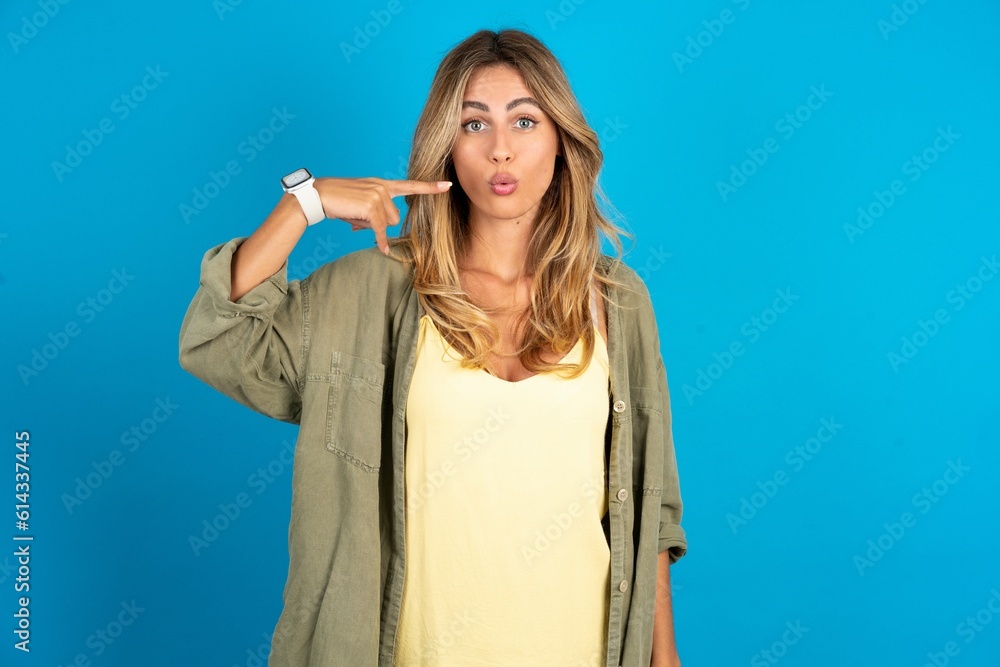 Charming young beautiful blonde woman wearing overshirt pointing on pout lips with forefinger, showing effect after lifting procedure, Charming young beautiful blonde woman wearing overshirt pointing on pout lips with forefinger, showing effect after lifting procedure,