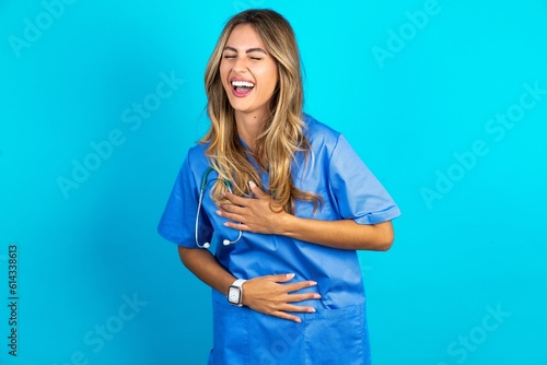 Young caucasian blonde doctor woman wearing blue uniform smiling and laughing hard out loud because funny crazy joke with hands on body.